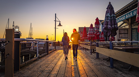 Two people walking along the boardwalk in Steveston at sunset